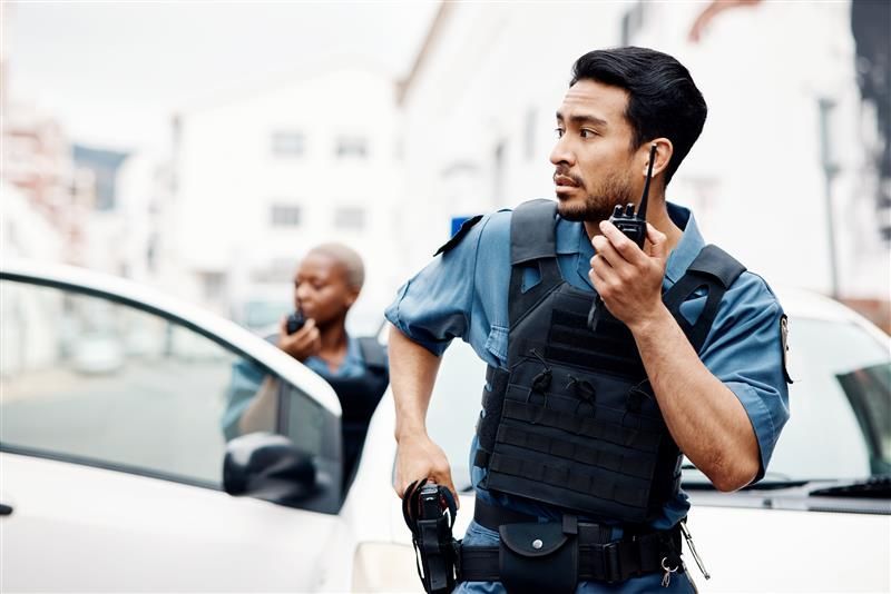 Police officers in a street, one looking right with a radio, the other in the background using a radio.