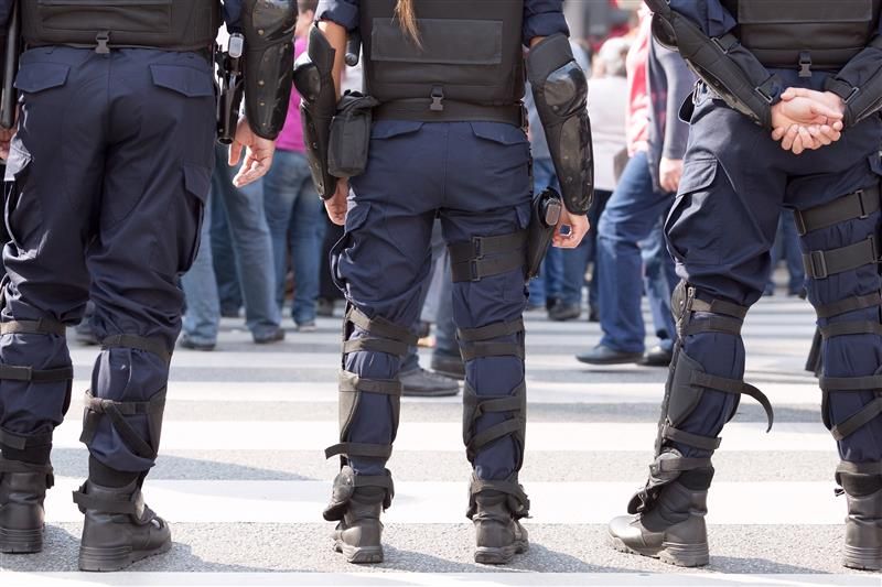 Police officers in tactical gear standing in front of a crowd at a crosswalk.