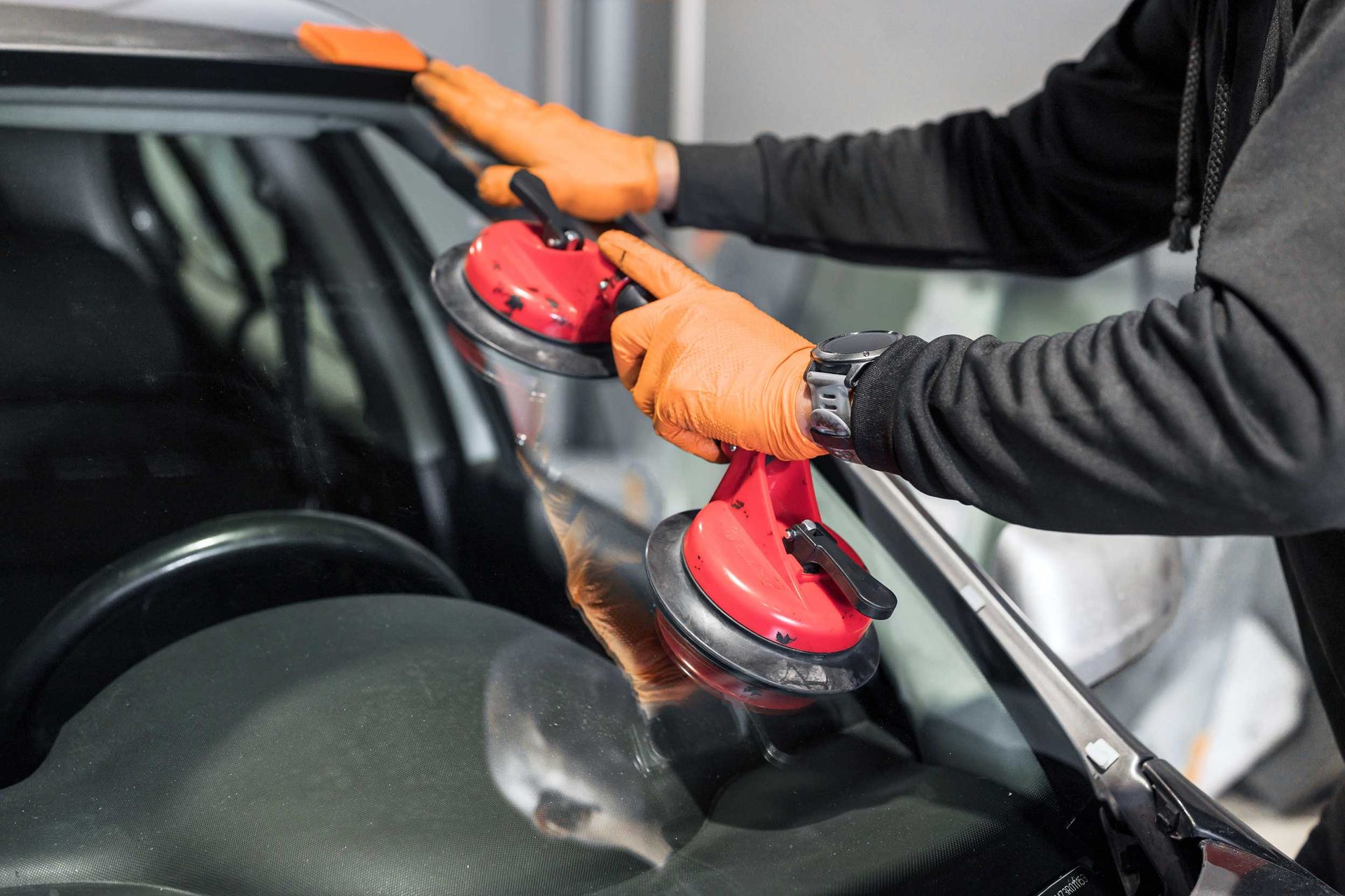 Gloved hands using a suction tool to install a car windshield.