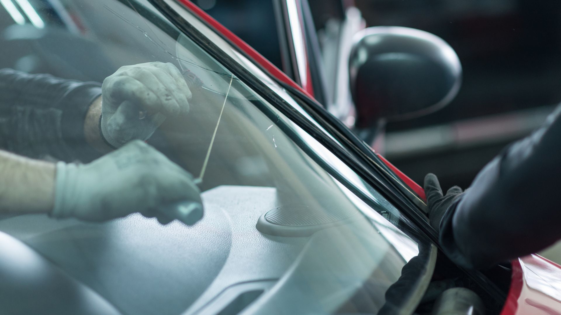 Two car mechanics remove a damaged windshield from a car, inside a car repair shop.