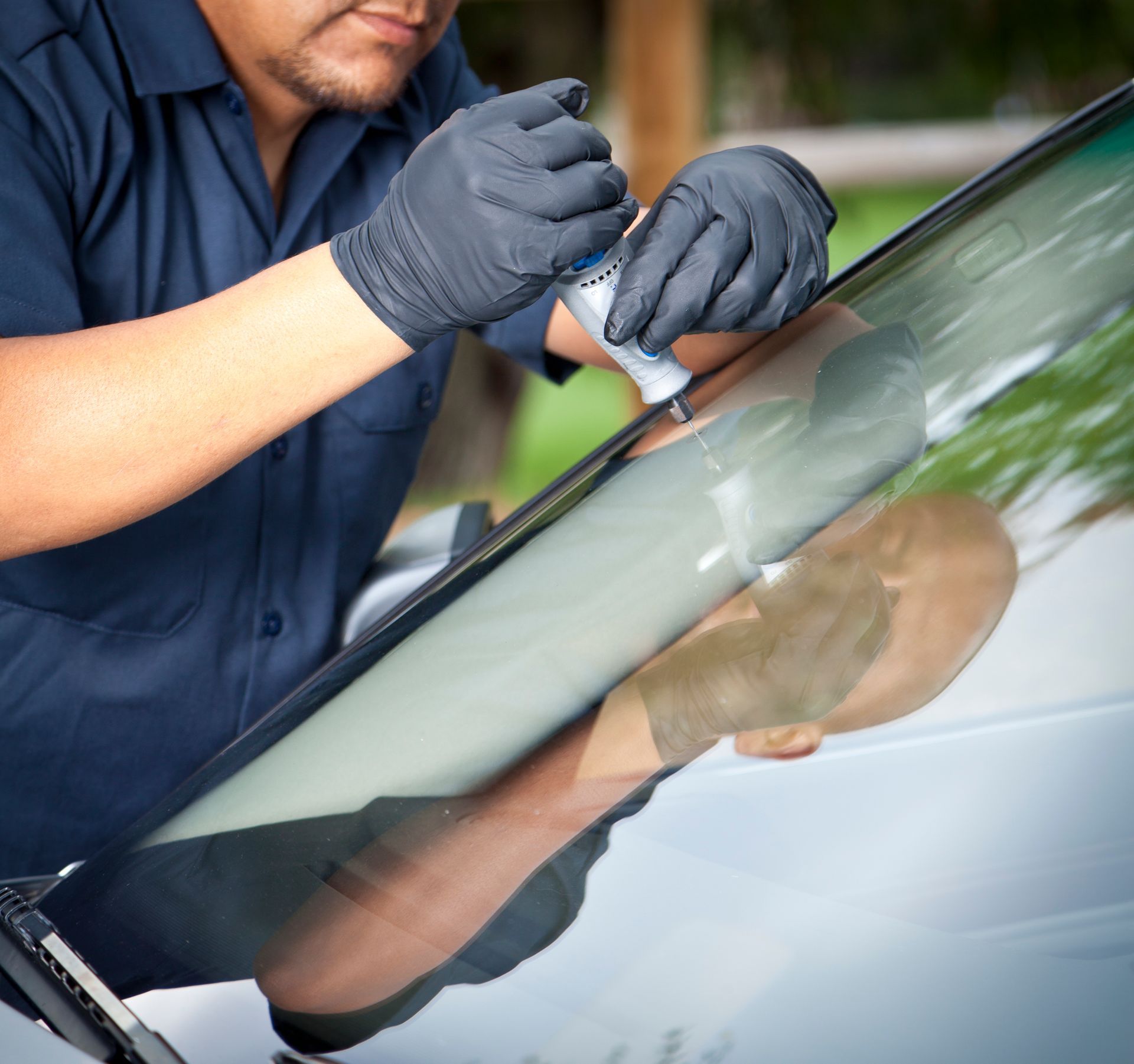A man in a blue uniform and black gloves fixes a windshield, showcasing car glass replacement.