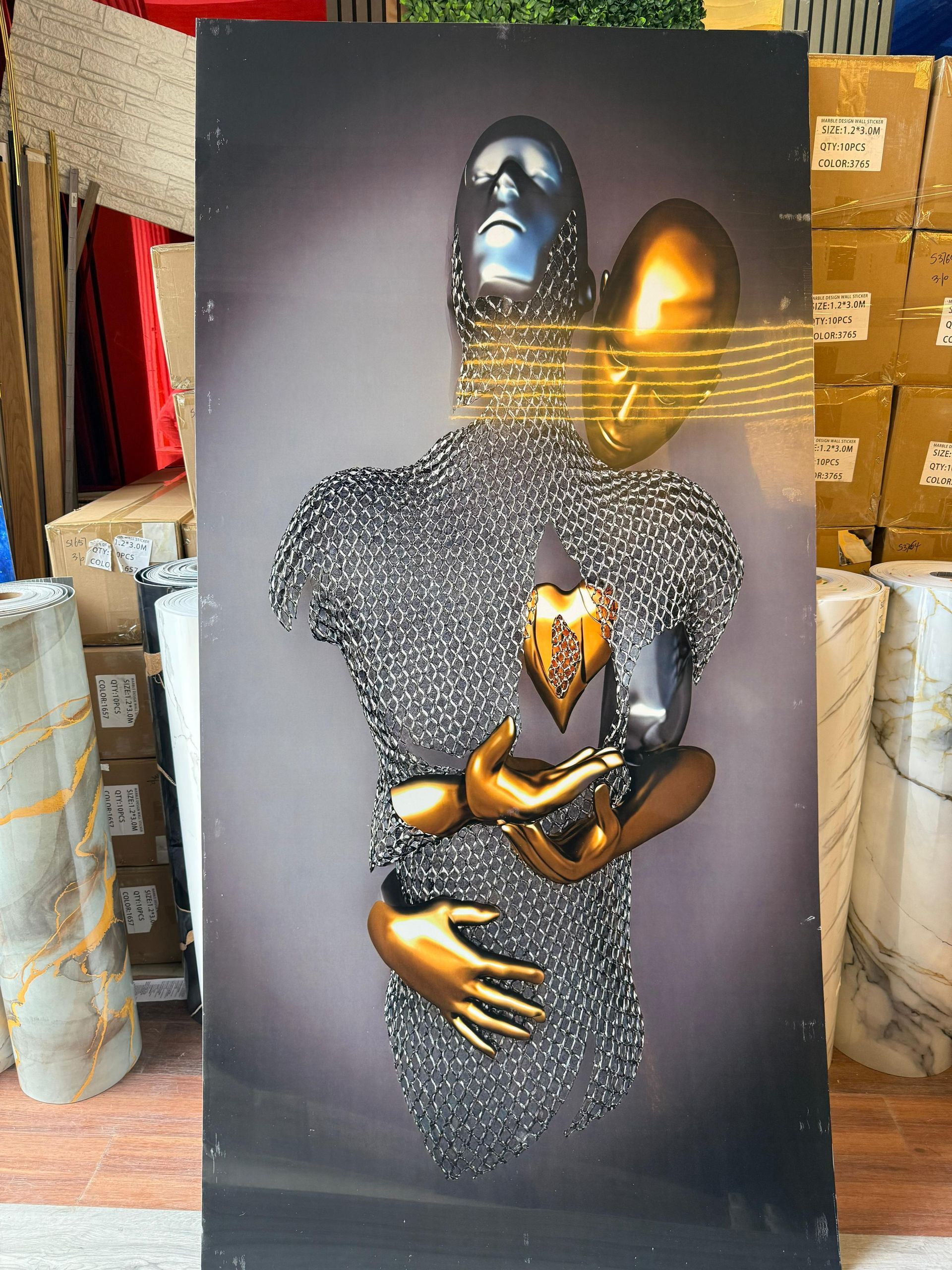 Obra de arte abstracta: figuras metálicas abrazadas, manos, corazón y rostro dorados. Tonos grises, dorados y plateados.