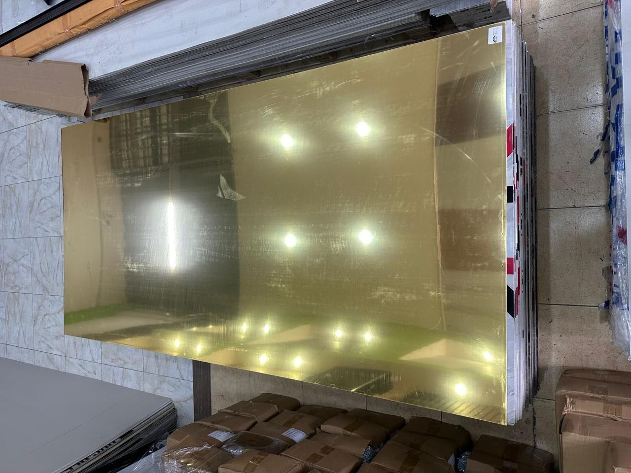 Una gran lámina reflectante de color dorado, apilada sobre un palé, bajo luces brillantes.