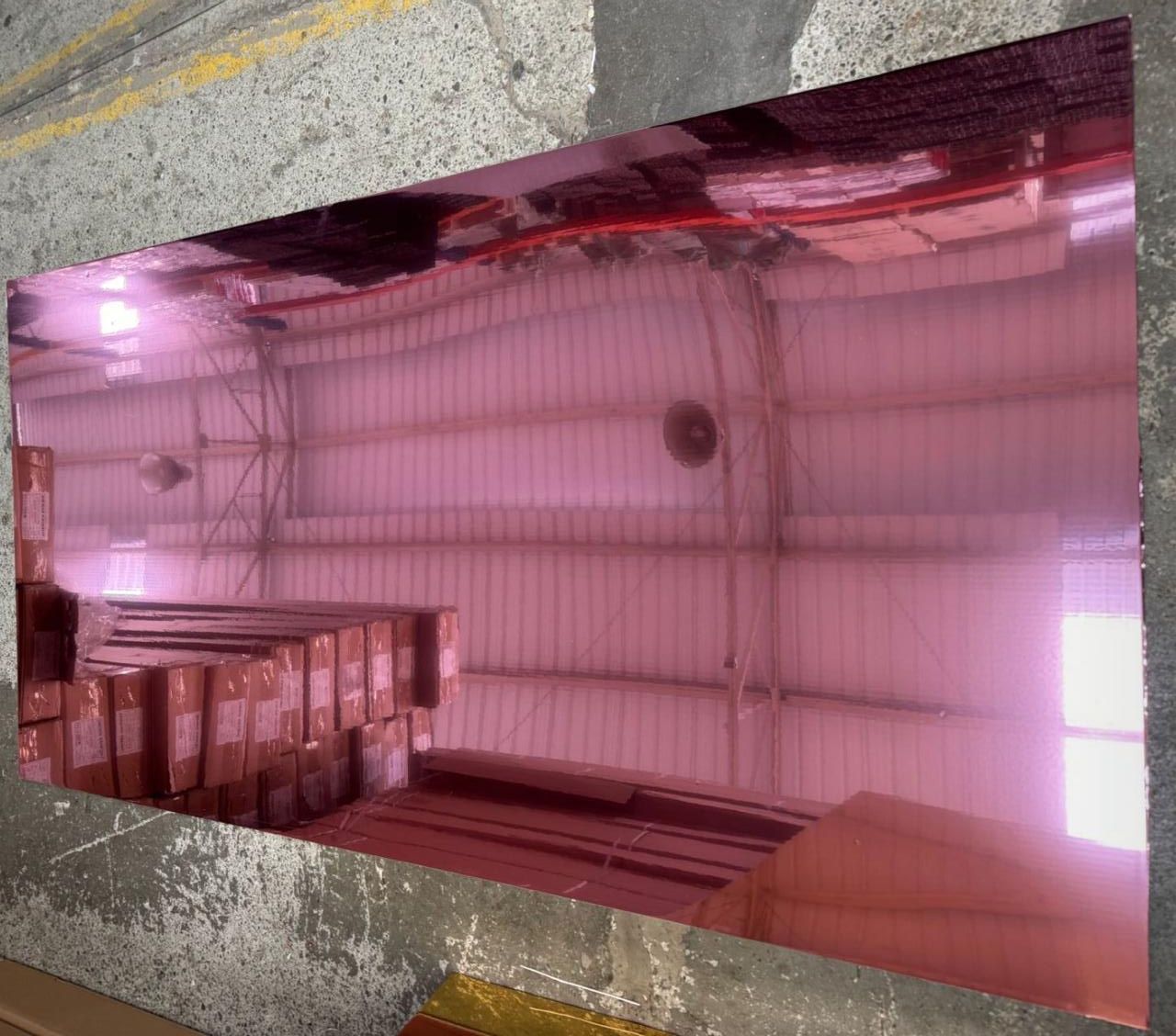 Lámina metálica reflectante rosa que refleja el interior de un almacén con pilas de cajas.