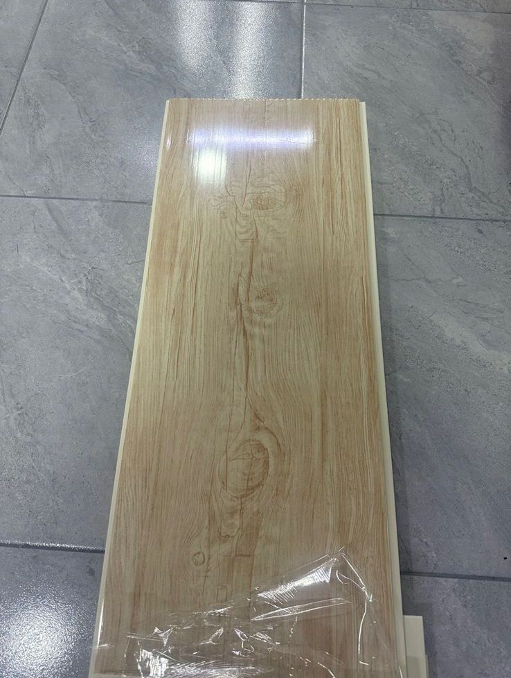 Tablón de madera de color claro con veta de madera, envuelto en plástico transparente, apoyado sobre una superficie alicatada.