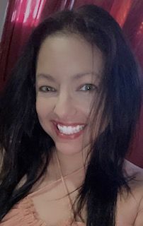 Woman with long dark hair smiles brightly, wearing a light-colored top. Pink background.