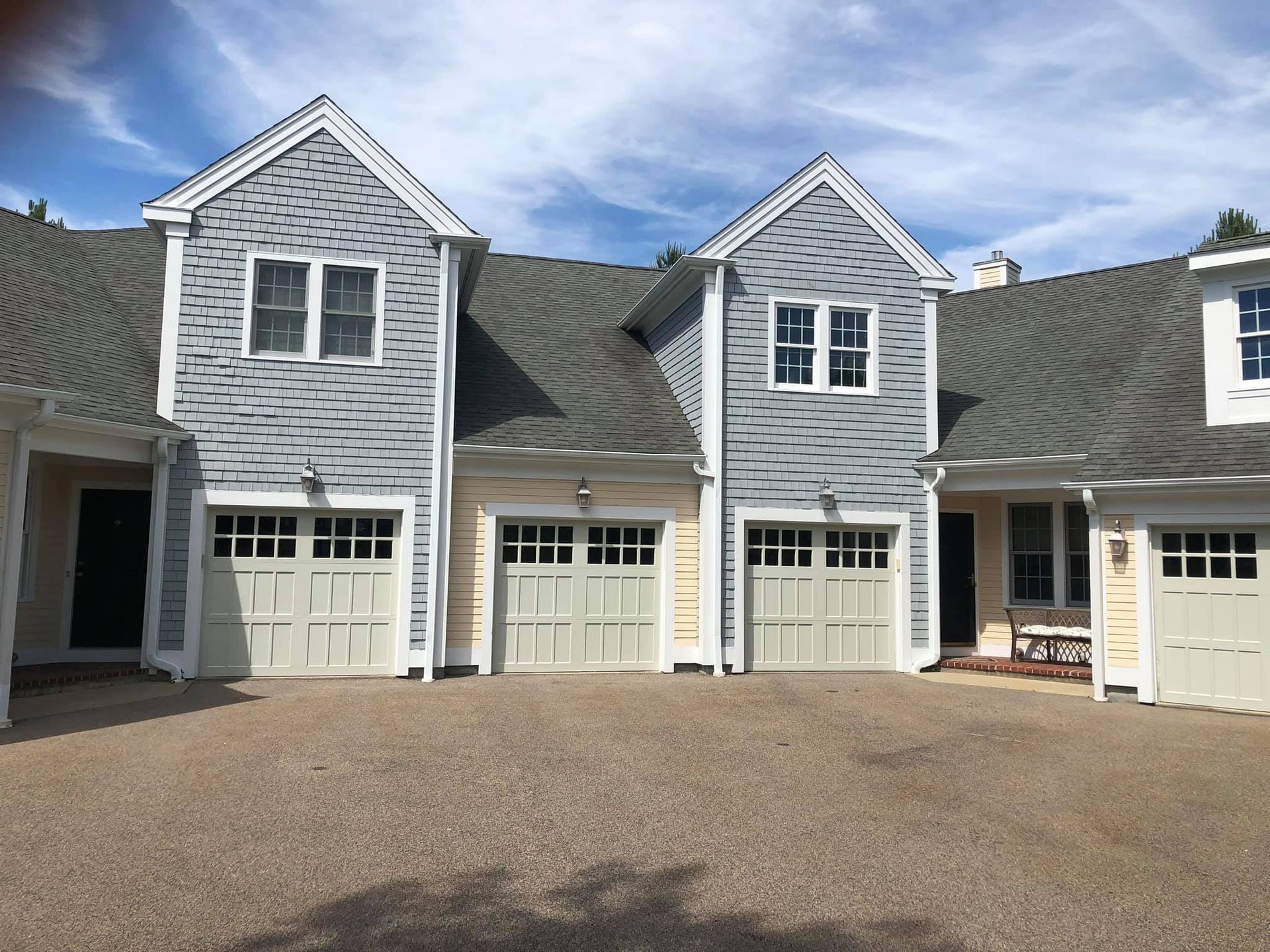 Multi-unit residential complex with light blue and yellow siding, beige garage doors, and gravel driveway.