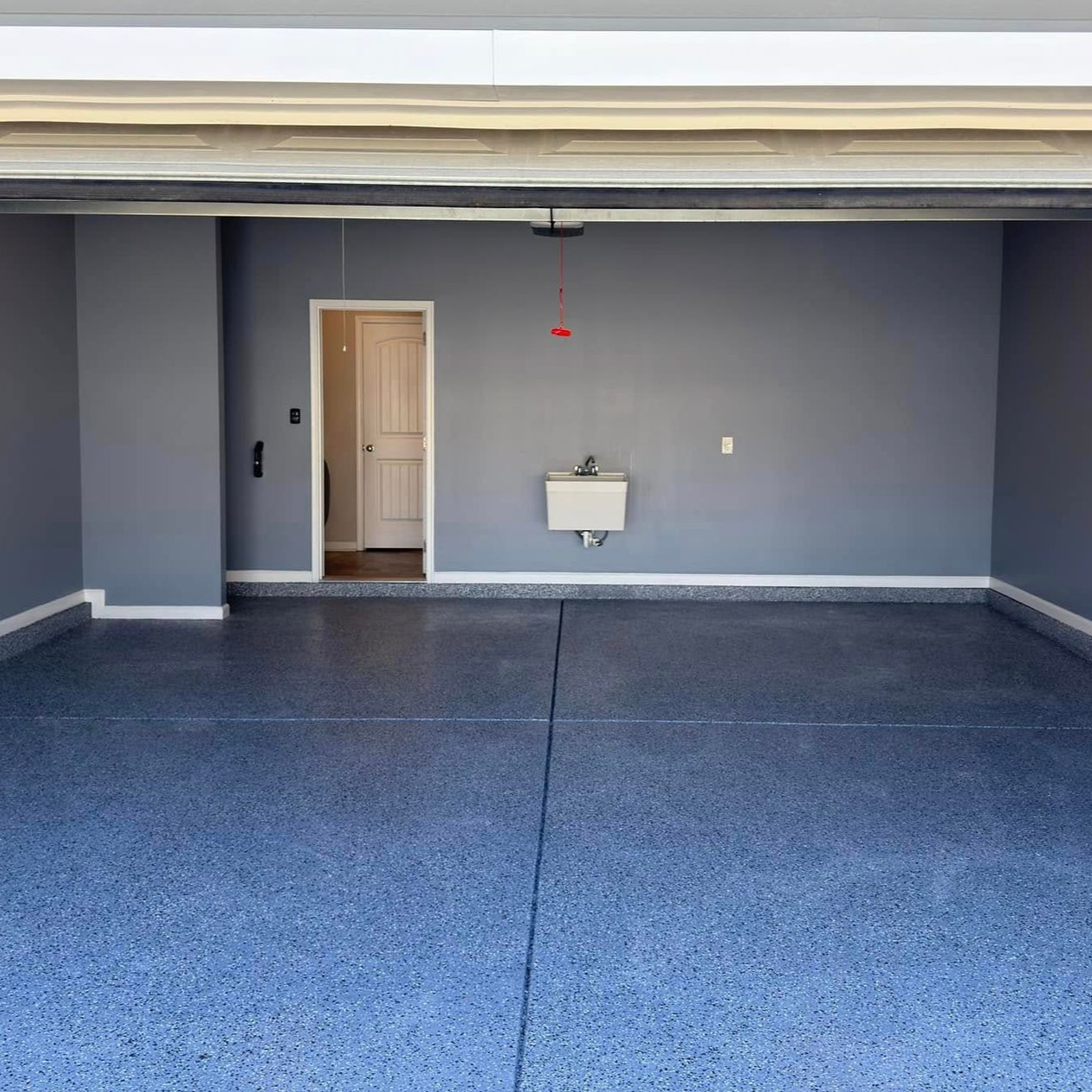 Empty garage with blue speckled floor, gray walls, and a utility sink.