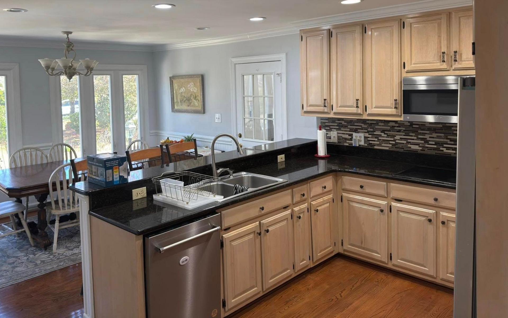 Kitchen with light wood cabinets, dark countertops, stainless steel appliances, and a dining area.