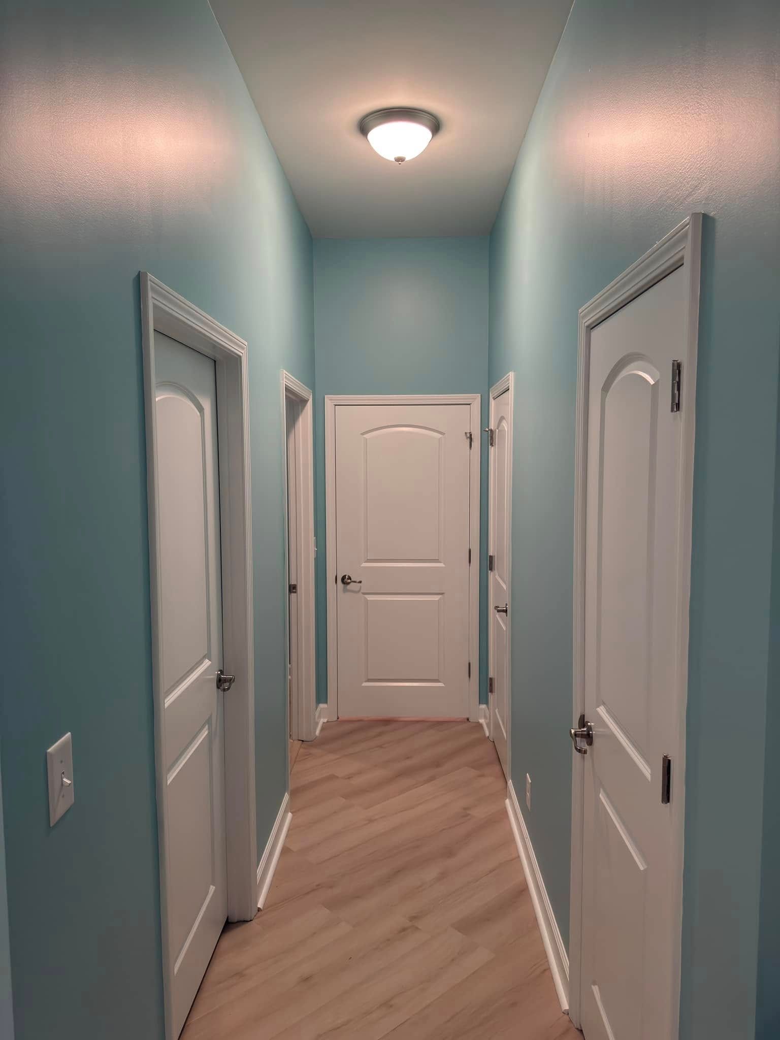 Narrow hallway with light blue walls, white doors, and a wood-look floor.
