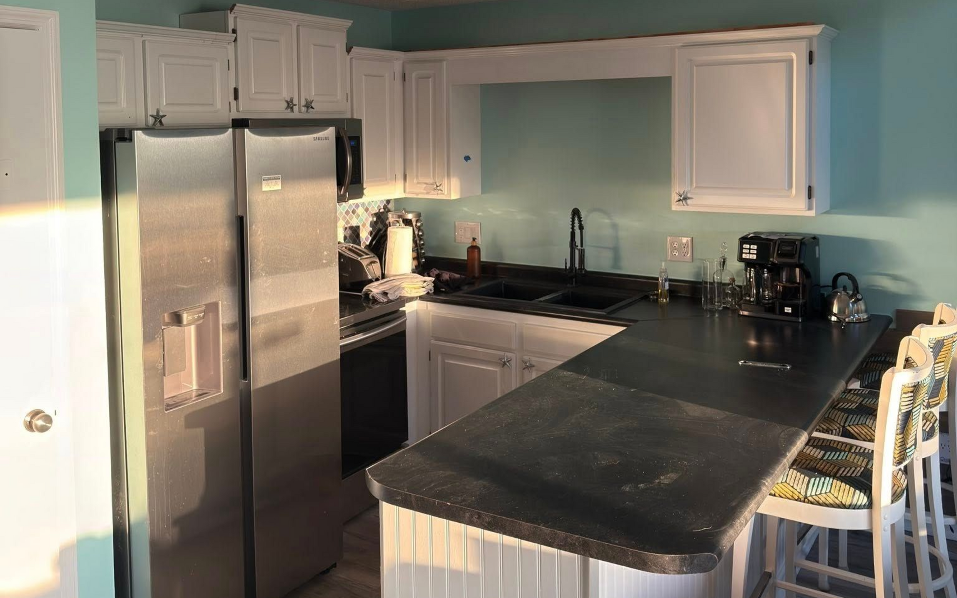 Kitchen with white cabinets, stainless steel appliances, black countertops, and a breakfast bar.