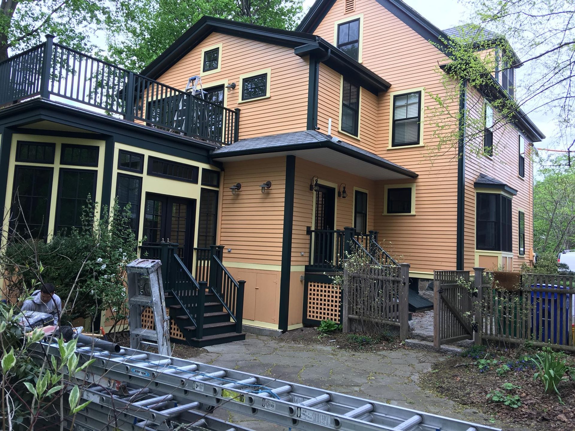 Two-story yellow house with black trim and porch, ladder in front.