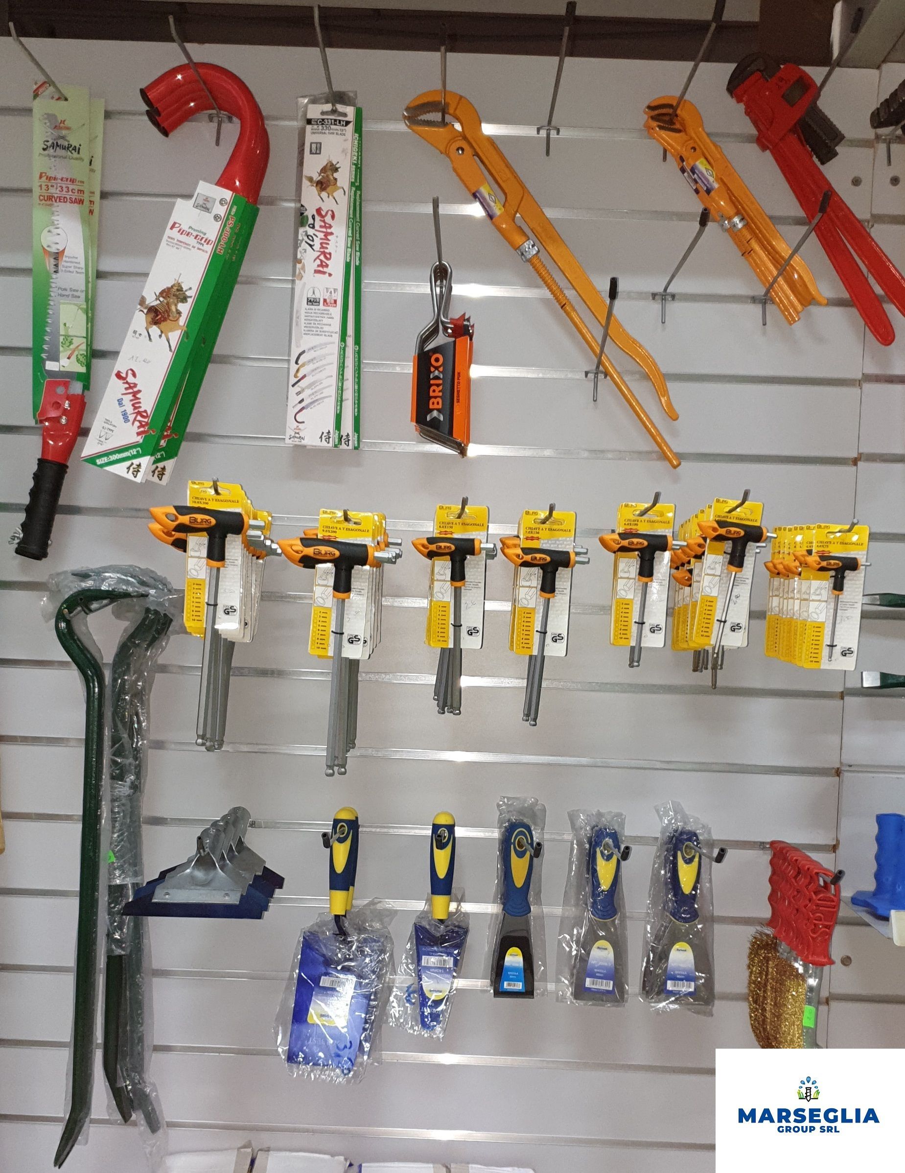 Attrezzi esposti su una parete bianca, tra cui seghe, chiavi inglesi e altri utensili.