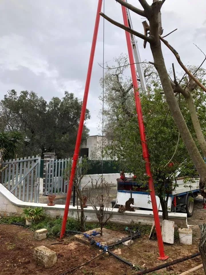 Attrezzatura di perforazione a torre rossa installata in un cortile accanto a un albero, tubi e un camion.