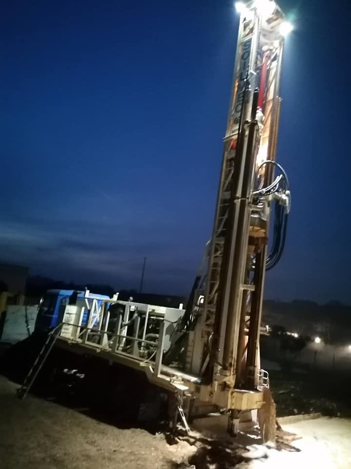 Piattaforma di perforazione illuminata di notte, al lavoro in un'area aperta con cielo azzurro.