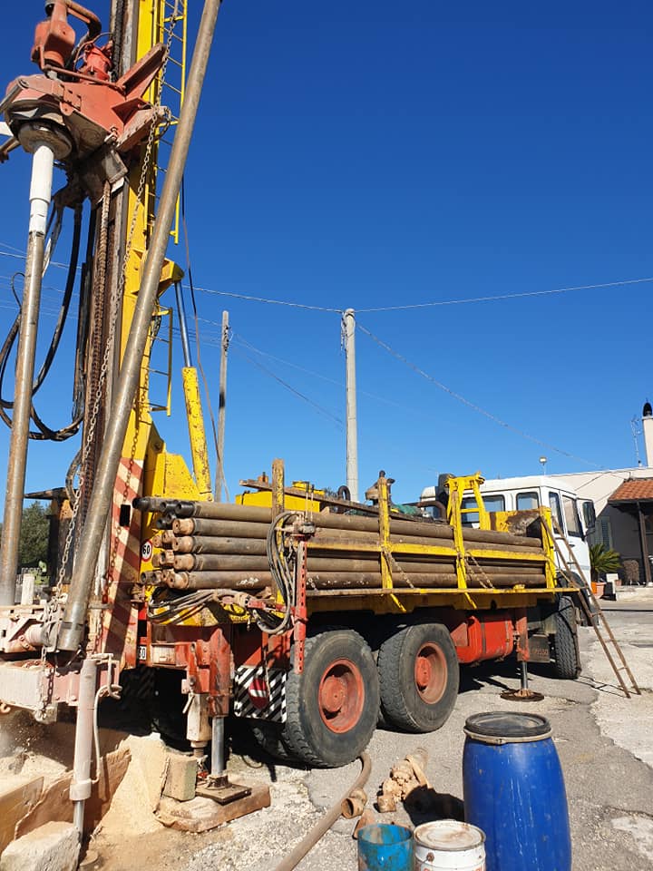 Una piattaforma di perforazione su un camion, con macchinari gialli e rossi che si stagliano contro il cielo azzurro. Sono visibili i tubi nel cassone.