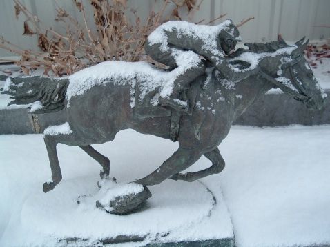 A statue of a jockey riding a horse covered in snow
