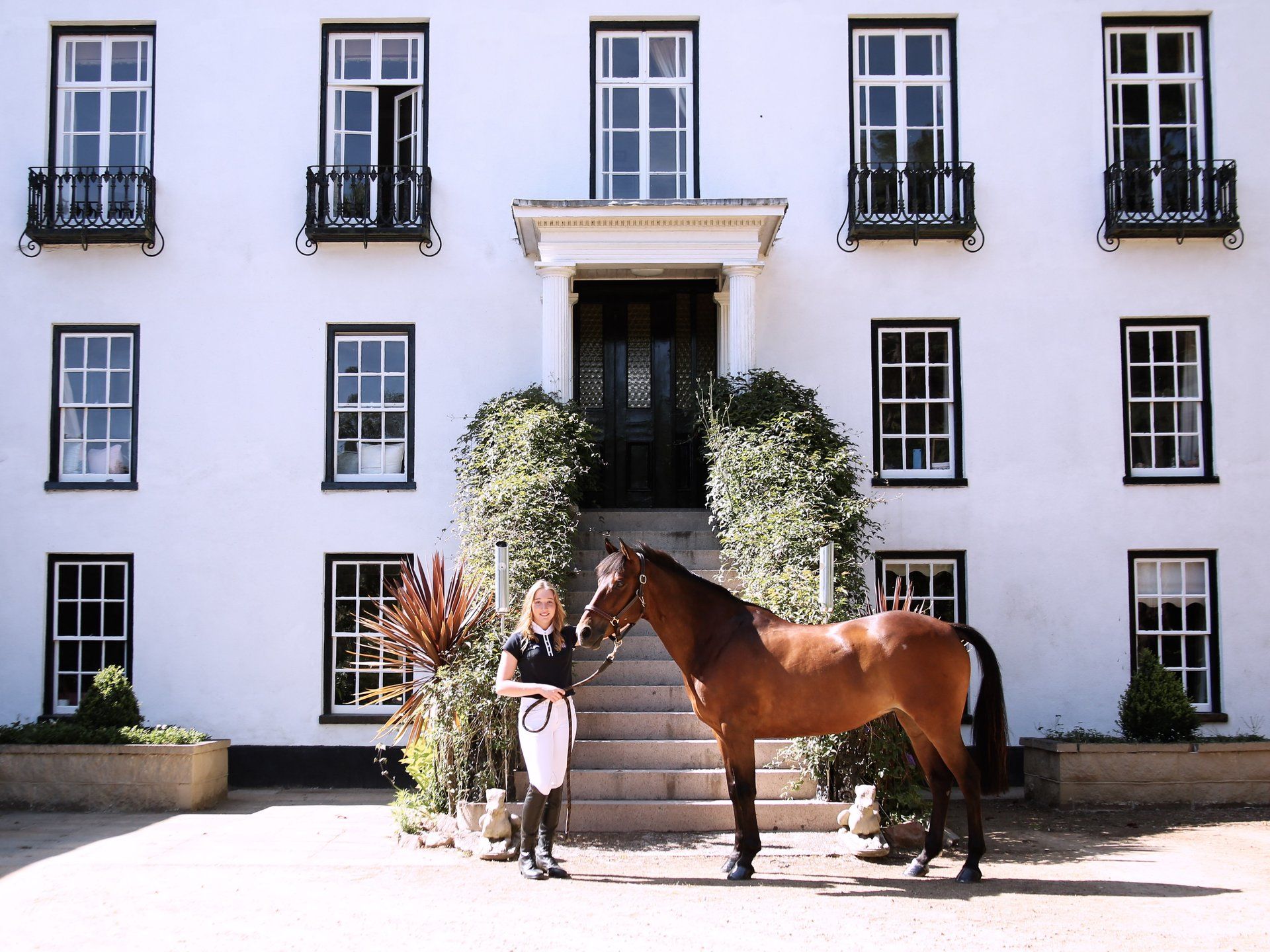 Woman and horse pose in front of a white building with black framed windows.