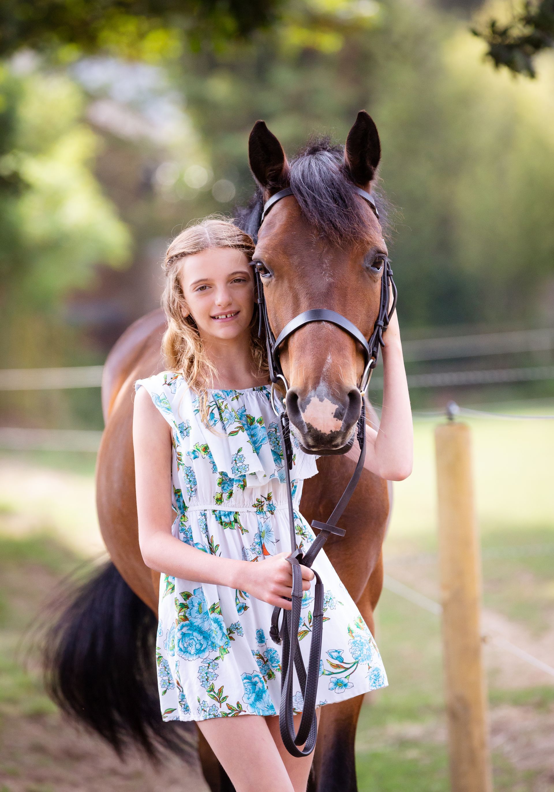 Girl in floral dress with brown horse in outdoor setting.