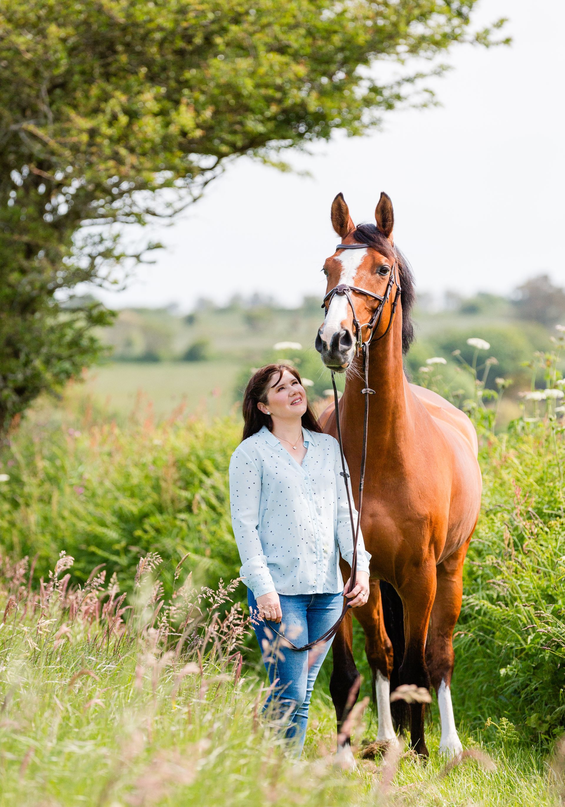 Woman with brown horse in a field, smiling, standing next to the animal.