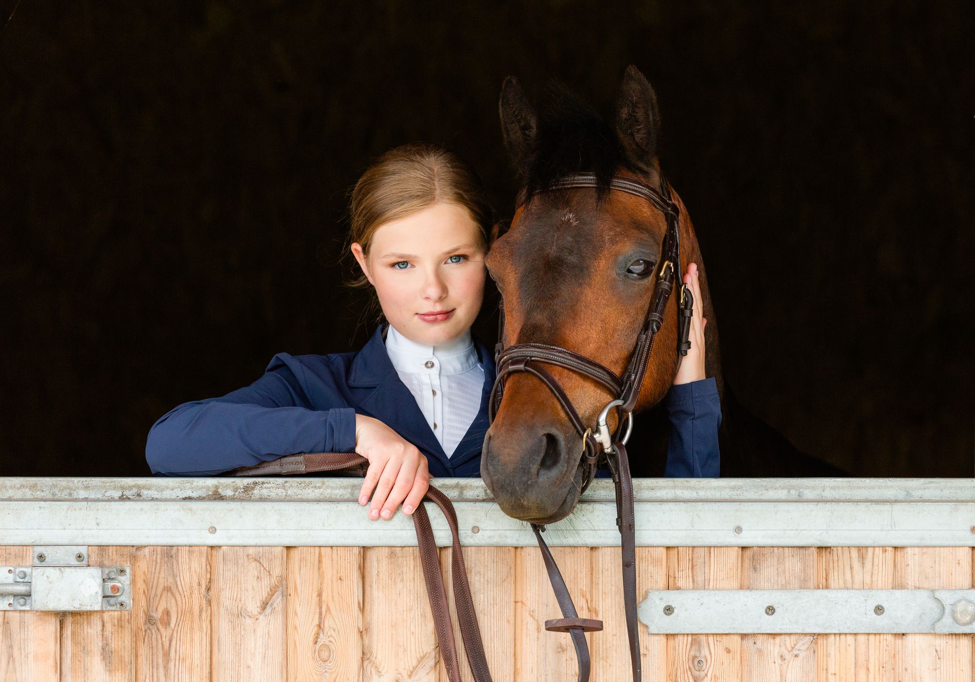 Woman in a blue jacket with a brown horse in a stable.