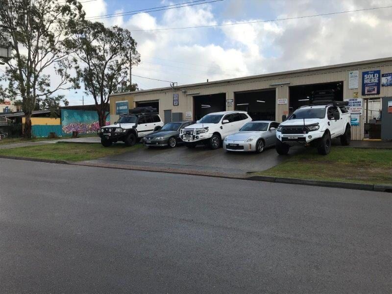 Cars Parked in Front of a Garage, Some Raised Trucks and Two Sports Cars, a Cloudy Day — Mike's Automotive in Edgeworth, NSW