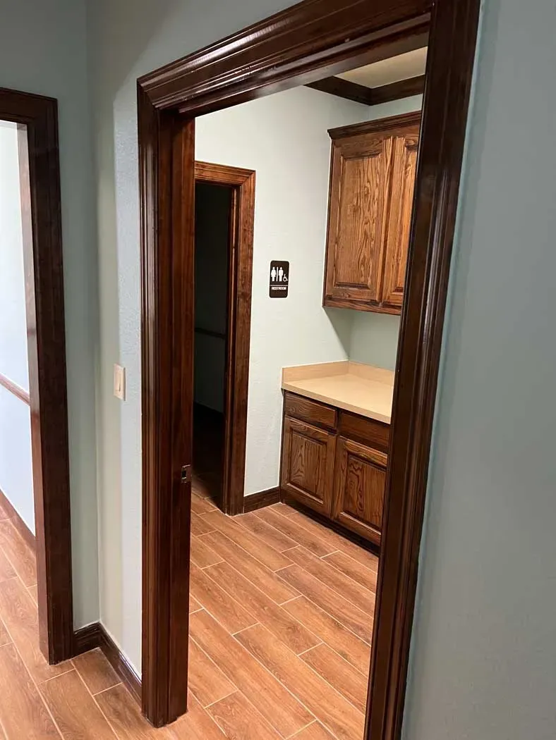 Hallway with wooden trim and doors leading to a room with cabinets and a counter.