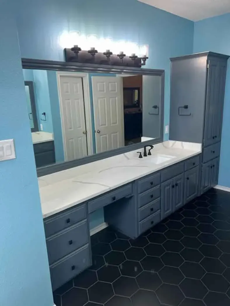 Blue bathroom with long vanity, black hexagonal tile floor, and tall storage cabinet.