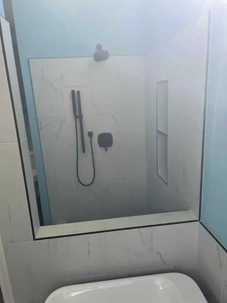 Modern shower with white marble-look tile, black fixtures, and a recessed shelf. Bright light reflects off the surfaces.