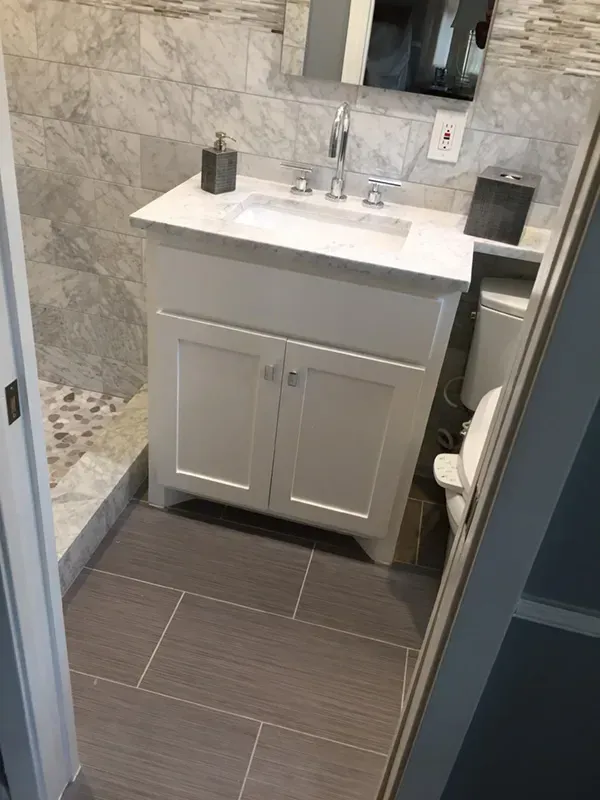 White vanity with sink, gray tiled floor and shower in a bathroom.