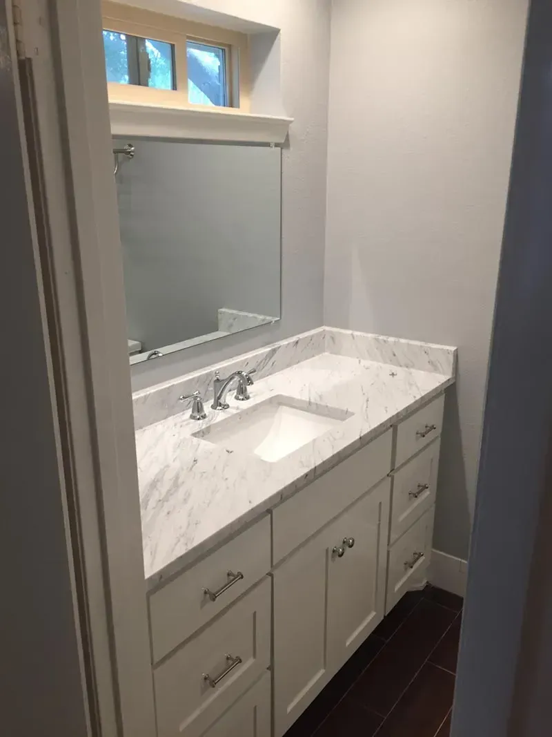 White bathroom vanity with marble countertop, silver faucet, and mirror.