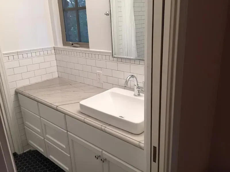 Bathroom with white cabinets, countertop, sink, and subway tile, with a window and mirror.