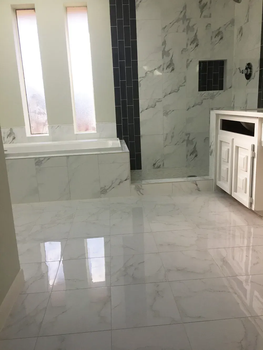 Bright, modern bathroom with white marble tile, bathtub, and vanity. Large windows provide natural light.
