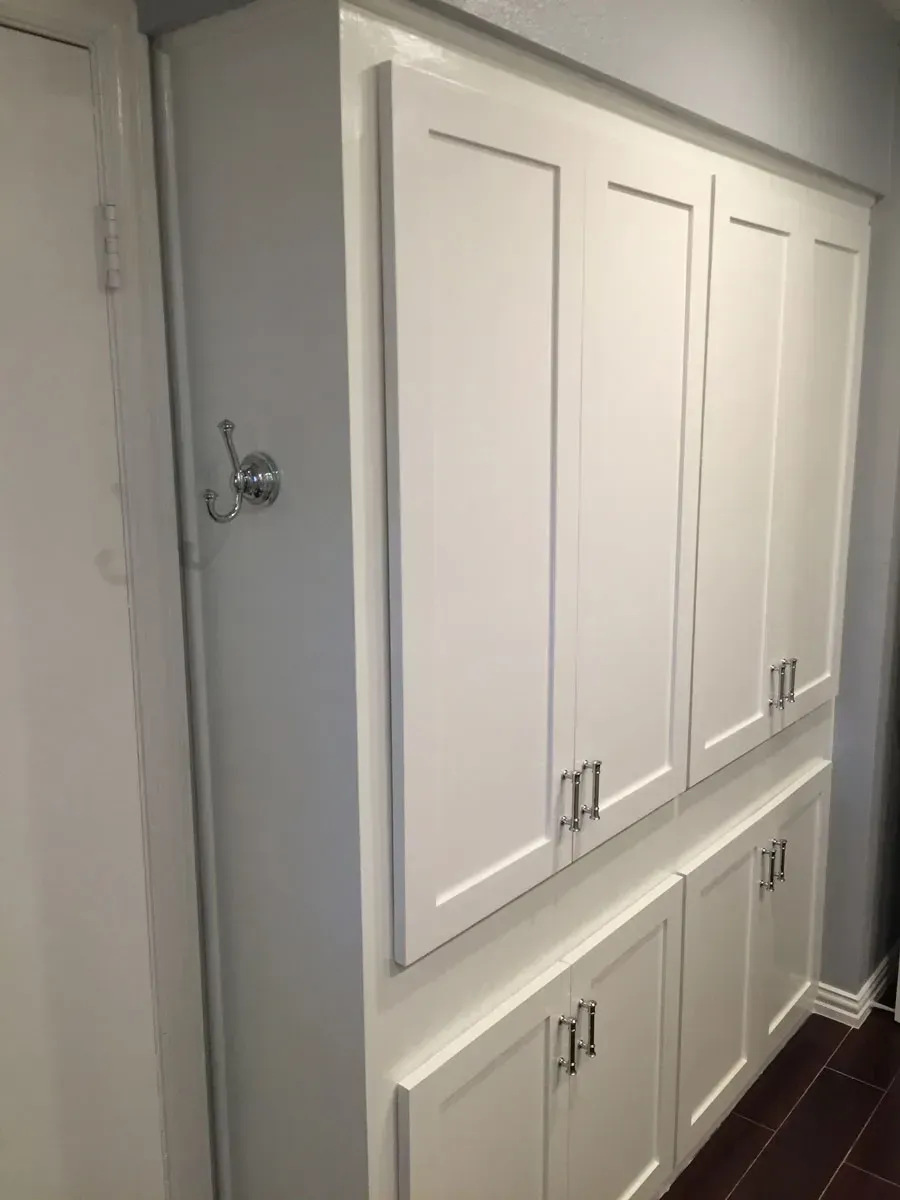 White built-in cabinets with silver handles. Next to a white door with a silver hook.