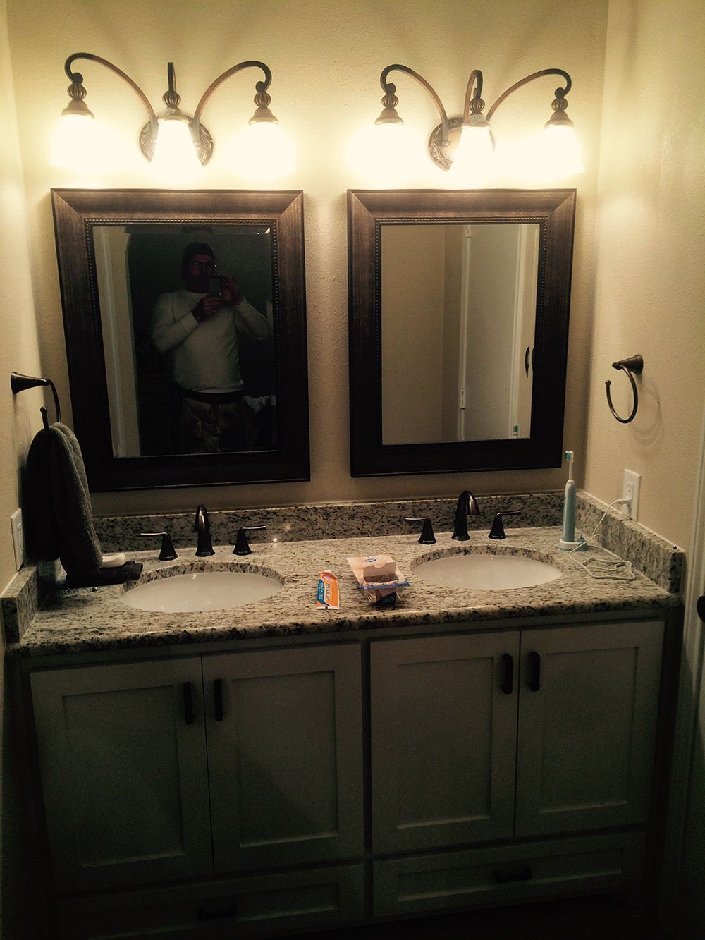 Bathroom vanity with two sinks, mirrors, and sconce lighting. A person is visible in the left mirror.