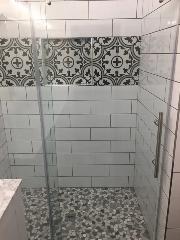 Shower with glass doors. White subway tiles, decorative black and white tiles, pebble floor.