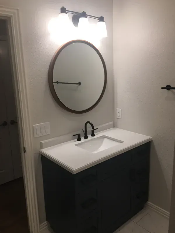 Bathroom with a black vanity, white countertop, round mirror, and black faucet.