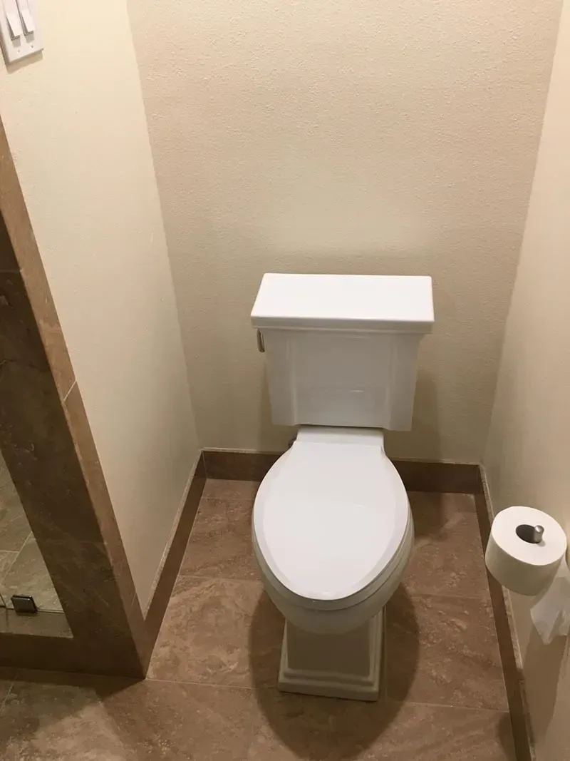 White toilet in a small bathroom with beige walls and brown floor tiles.