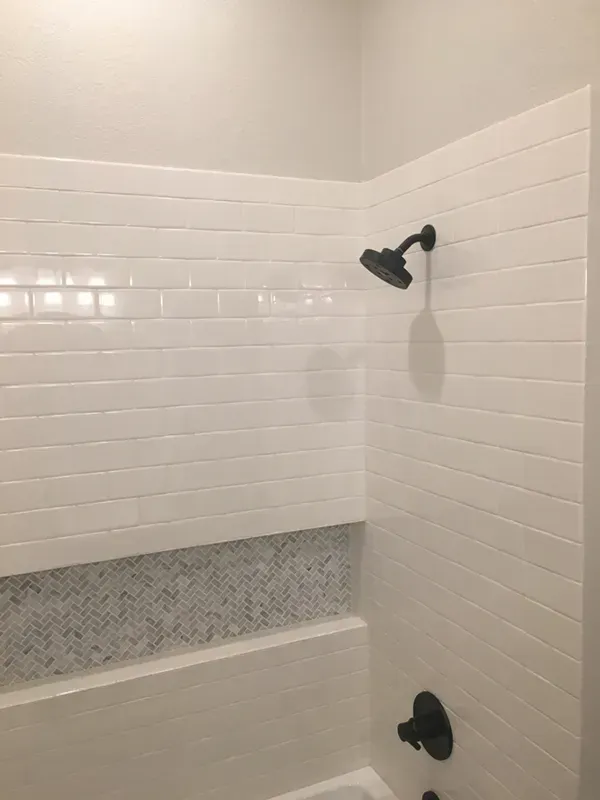 White tiled shower with black fixtures; the showerhead is mounted on a right wall.