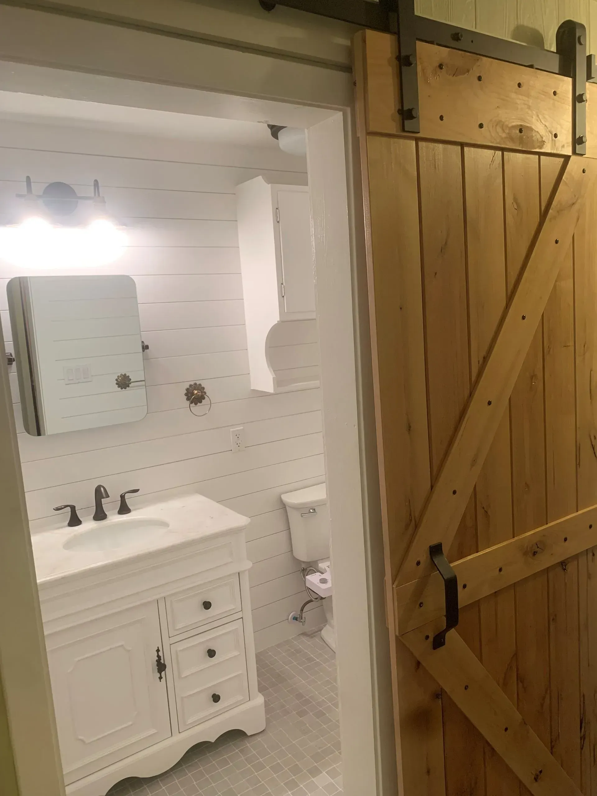 Bathroom interior with open wooden sliding barn door, white vanity, and shiplap walls.