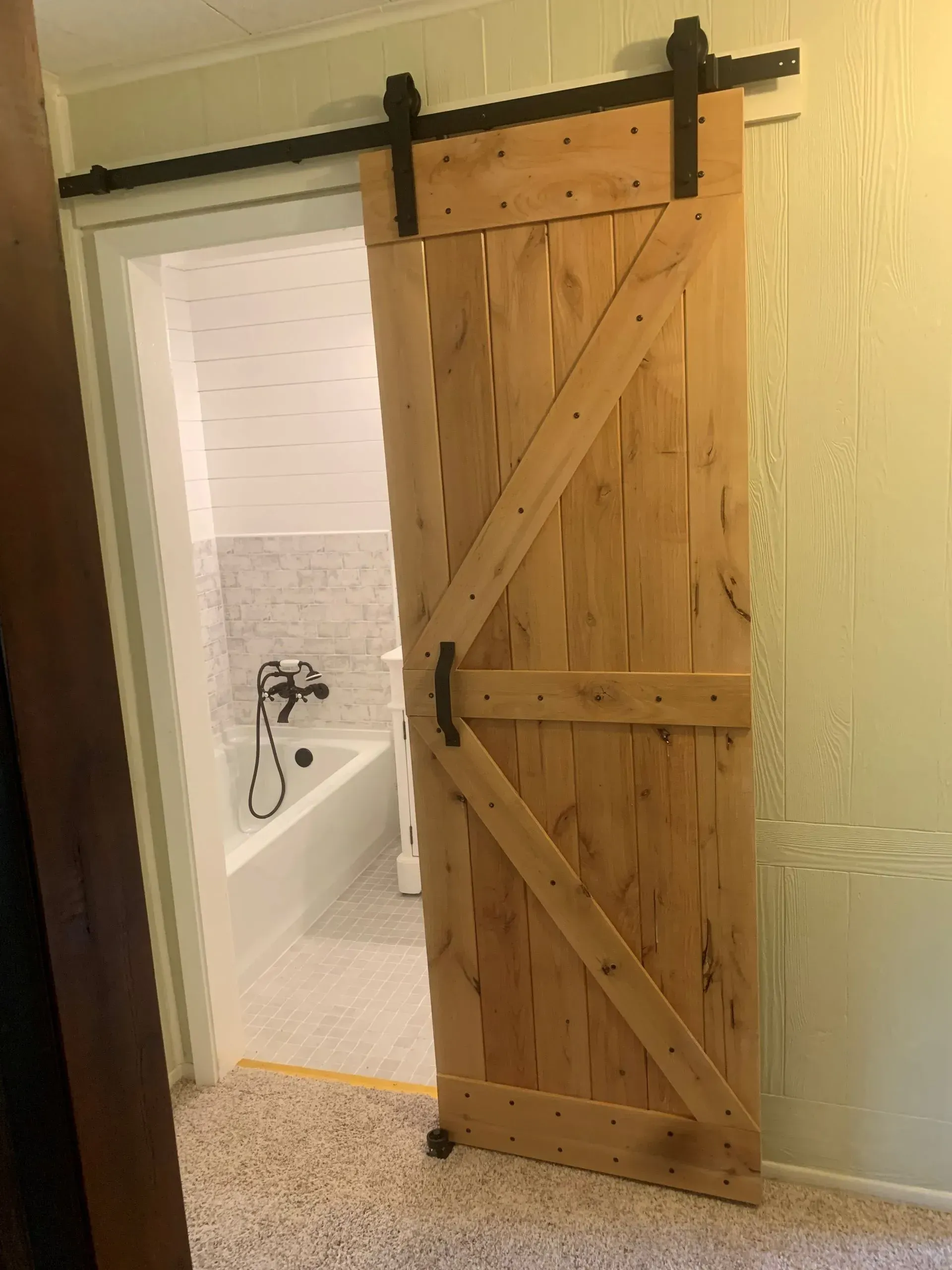 Wooden barn door partially open to a bathroom, with a black track and hardware.