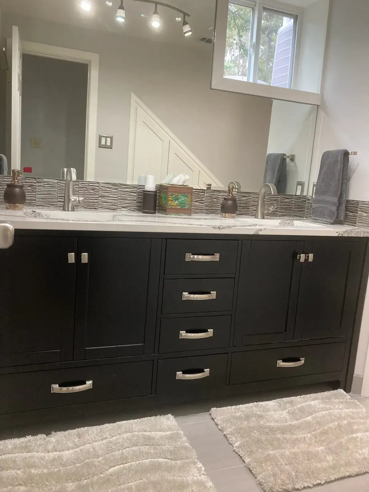 Black double bathroom vanity with marble countertop, silver fixtures, and mosaic backsplash.