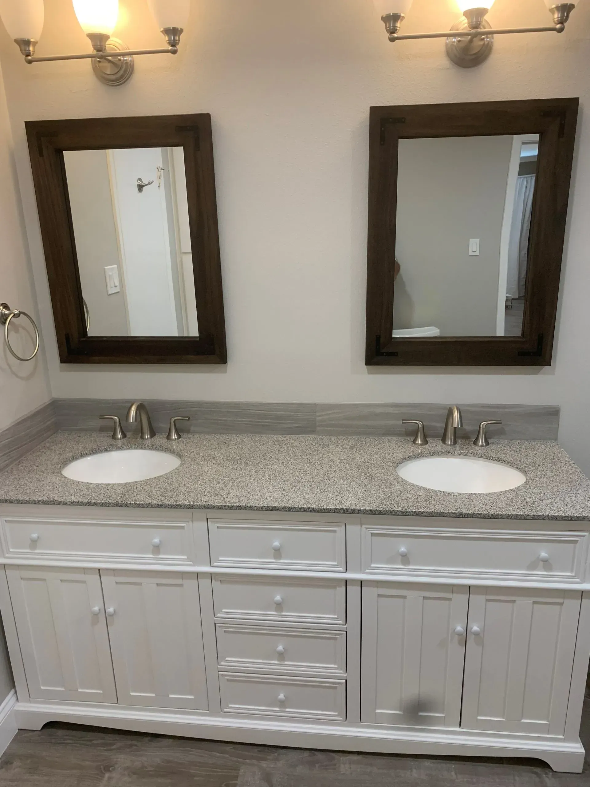 Double bathroom vanity with white cabinets, speckled countertop, two mirrors, and silver fixtures.
