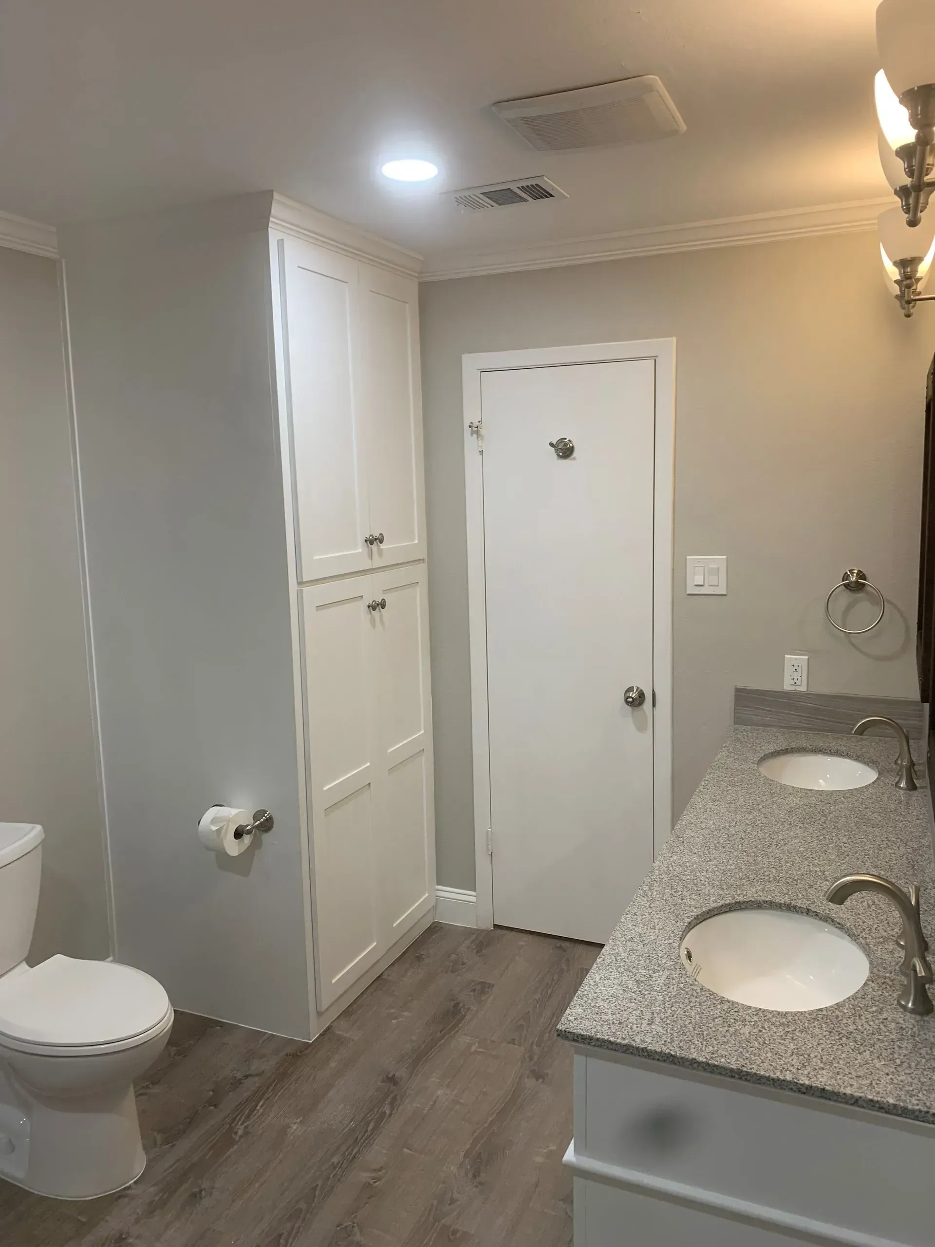 Bathroom with tall white storage cabinet, double sink vanity with granite countertop, and white door.