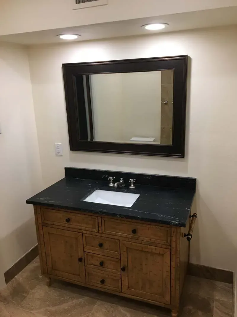 Bathroom with a wooden vanity, dark countertop, and large framed mirror.