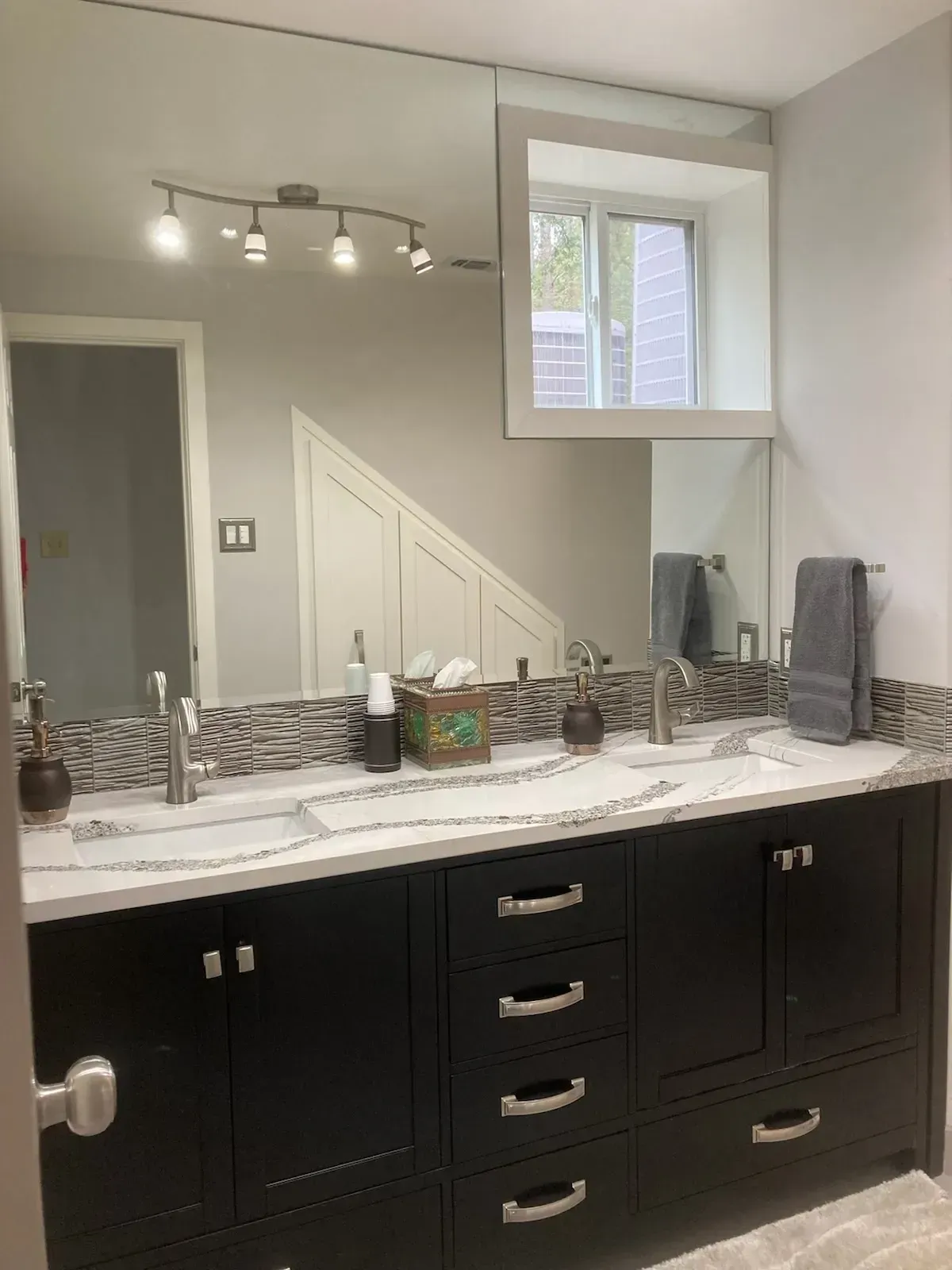 Black double sink vanity with a large mirror, lighting, and a small window in a bathroom.