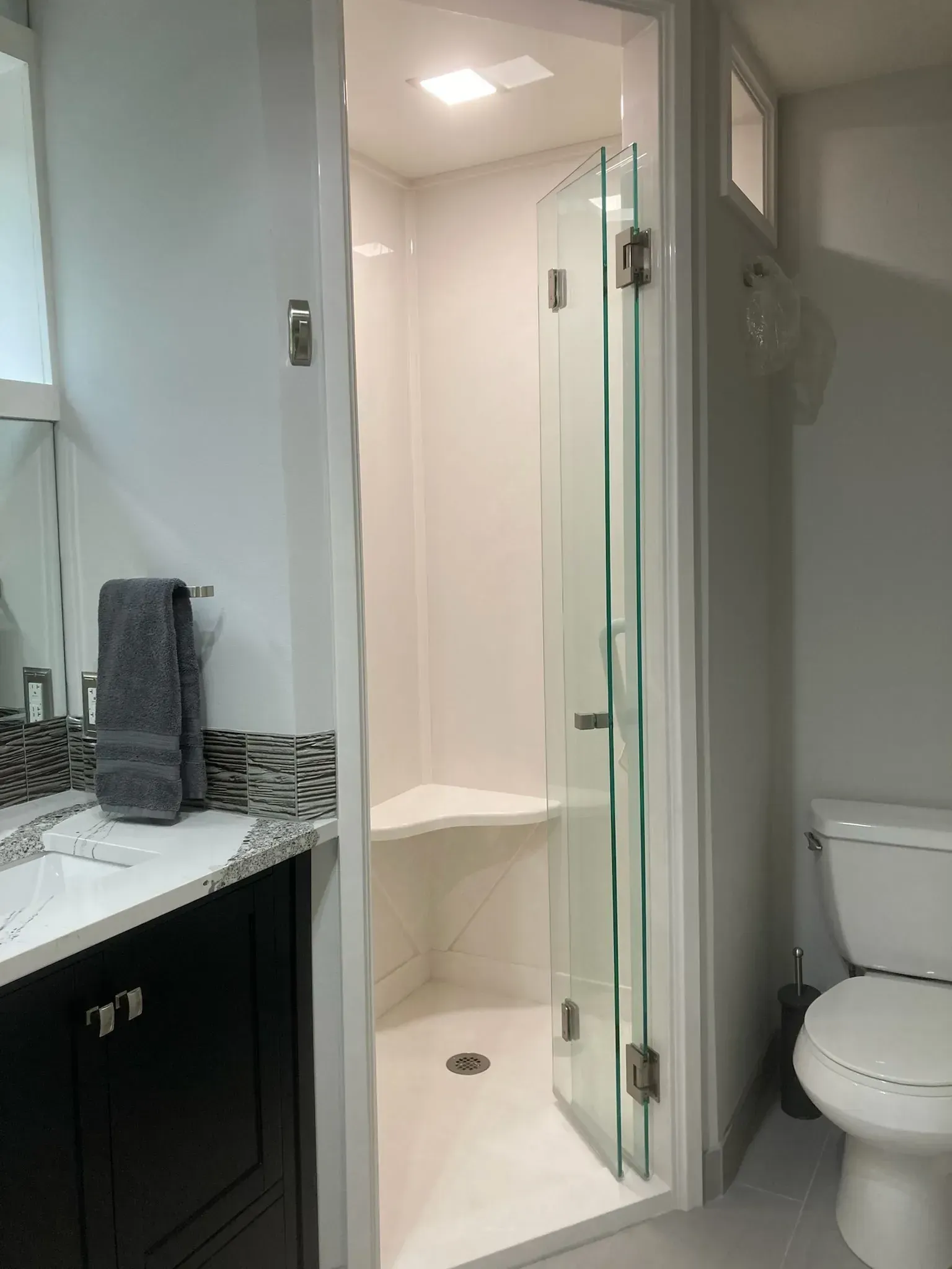 Small bathroom with white shower stall, glass door, toilet, and vanity with towel.