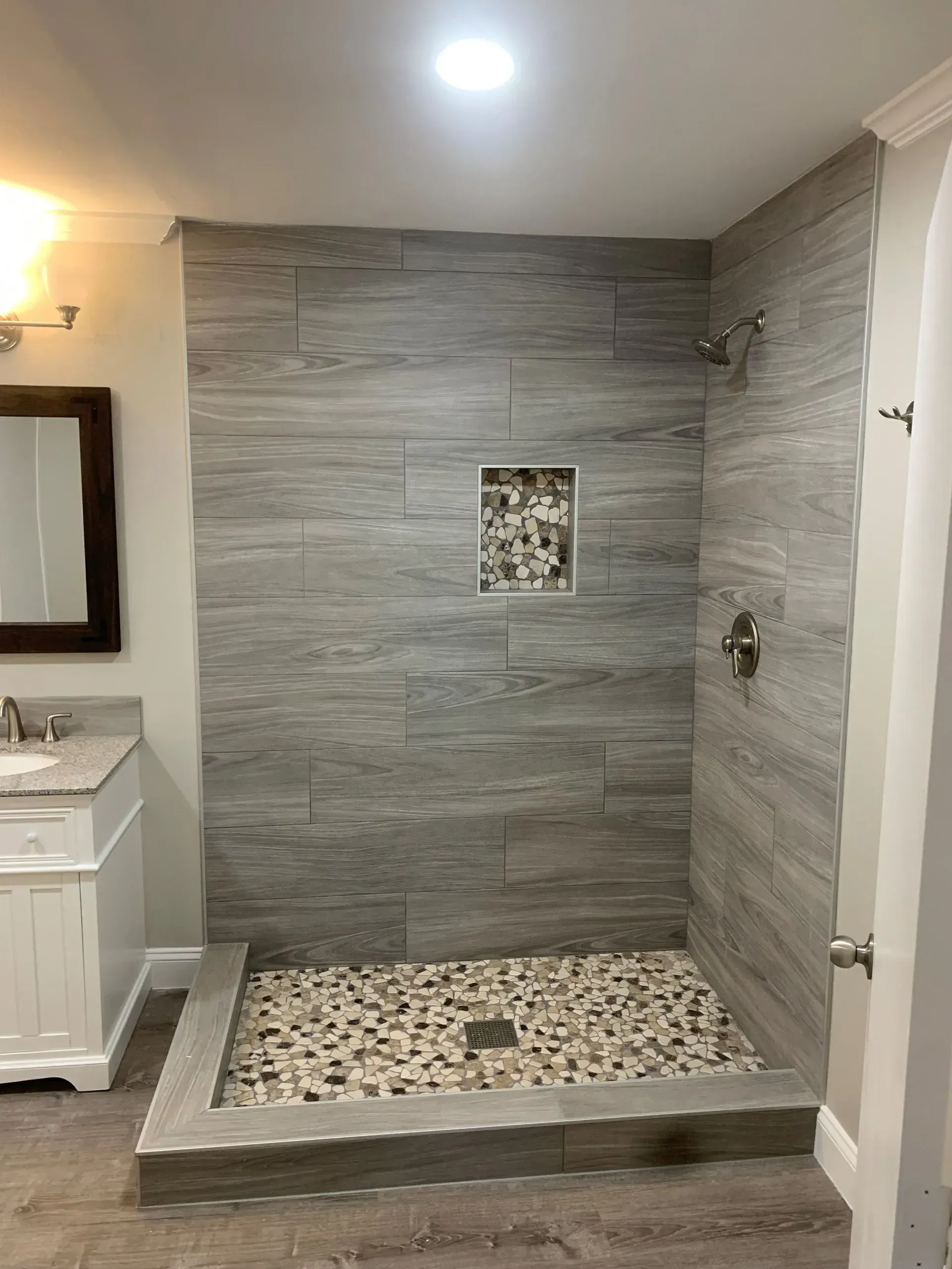 Bathroom with gray tile shower and pebble floor, recessed shelf, and silver fixtures.