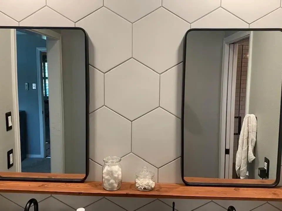 Bathroom with hexagon tile wall, two black-framed mirrors, wooden shelf, and decorative jars.