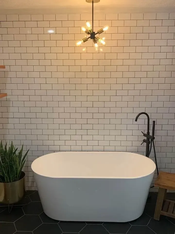 White oval bathtub against a brick-tiled wall, black floor, brass light fixture.